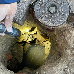 A worker shines a flashlight down a pothole to reveal a water service line.
