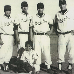 Four baseball players wearing Greeley Grays uniforms stand behind a kneeling bat boy.