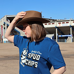 Person wearing blue t-shirt that has a cartoon of a potato on it wearing cowboy hat and boots and the words Mr. Spud Chips.