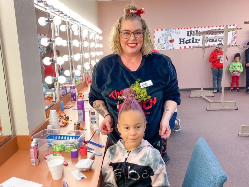 A volunteer creating fun hair designs on a young girl as part of the Whoville Holiday programming for Greeley’s Festival of Trees.