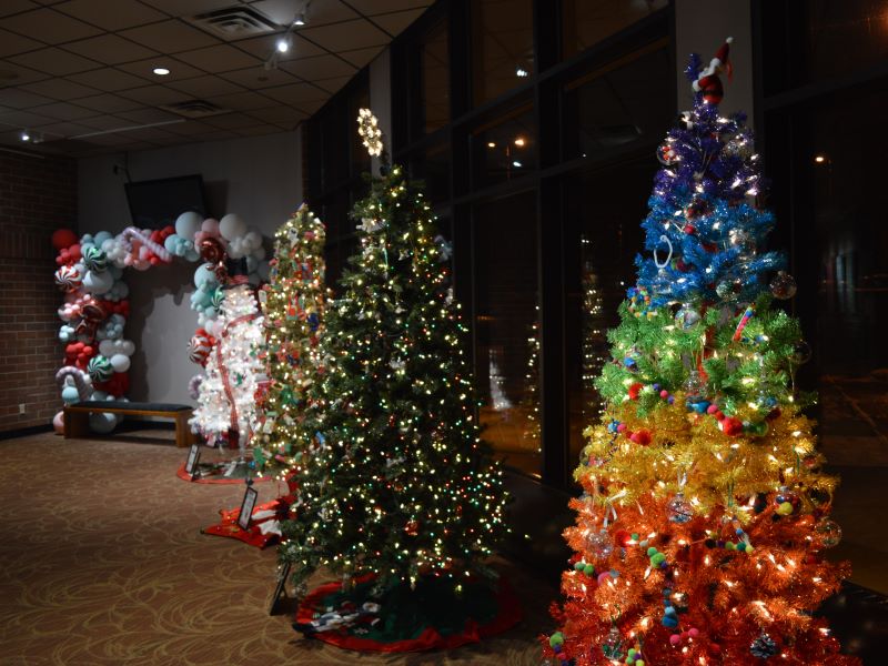 Several of the Festival of Trees displays in the Union Colony Civic Center lobby, including a balloon arch, a tree decorated like a snowman, and a rainbow tree.