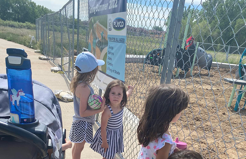 Photo of kids standing at fence observing playground rebuild