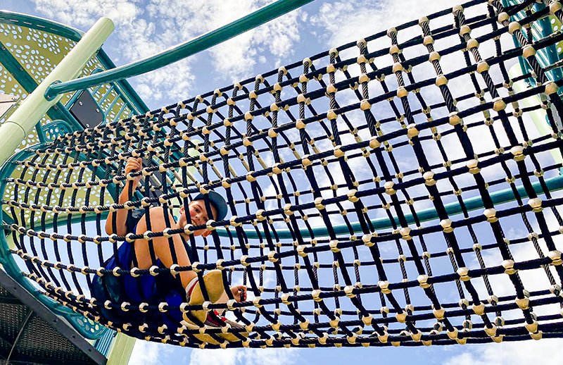 Photo of young boy climbing in rope ladder tube on playground