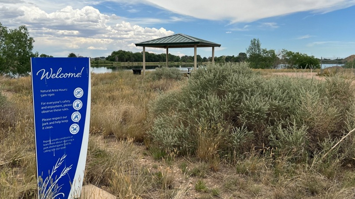 A blue sign reads &quot;Natural Area&quot; in front of a grassy pond