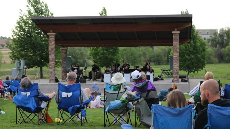 A crowd on lawn chairs face an outdoor stage where an ensemble is playing