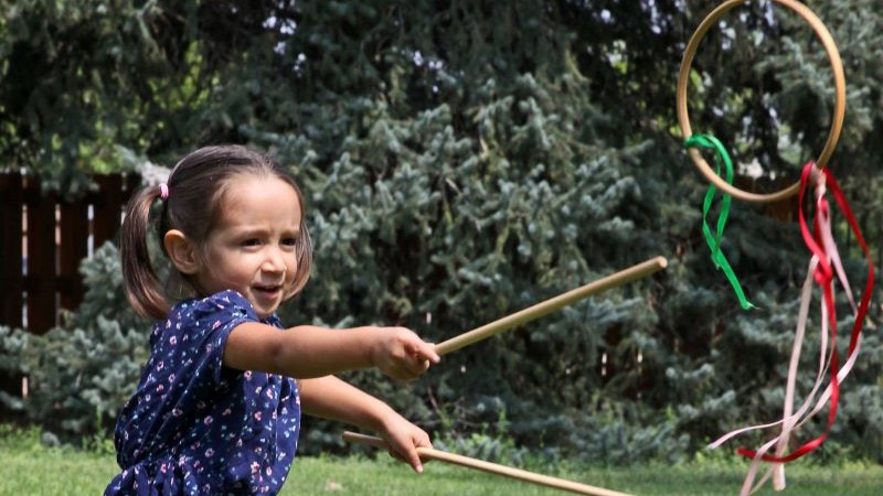 A child uses sticks to toss a wooden hoop