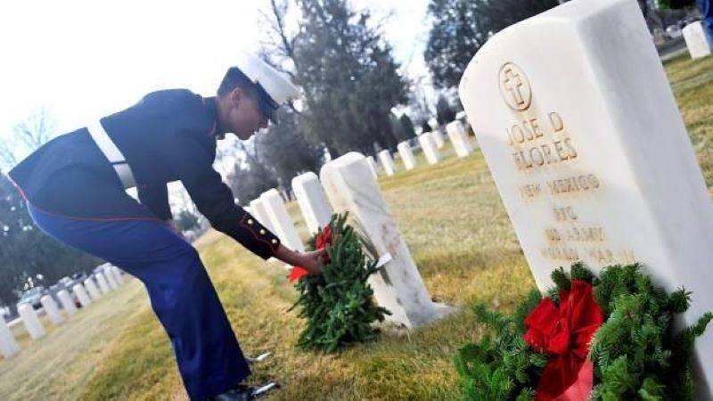 A Marine bends down to place a wreath on a gravestone during the Wreaths Across America ceremony at Linn Grove Cemetery.