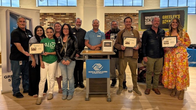 Group of eleven people stand in a row holding award plaques. There is a podium in the middle of the group that says Boys and Girl Club of Weld County.