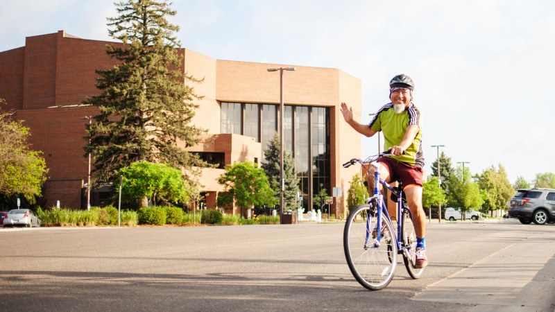 Man on bike waving as he rides by the Recreation Center in Greeley