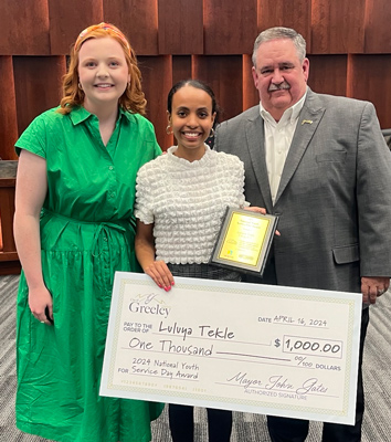 Mayor presenting oversized check in City Council chambers to a female high school student that won the 2024 National Youth Service Day Awards $1,000 scholarship.