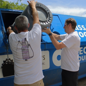 
Two O-I staff members empty a trash can full of glass bottles into a collection dumpster during a recycling drive at Crabtree Brewing Company.